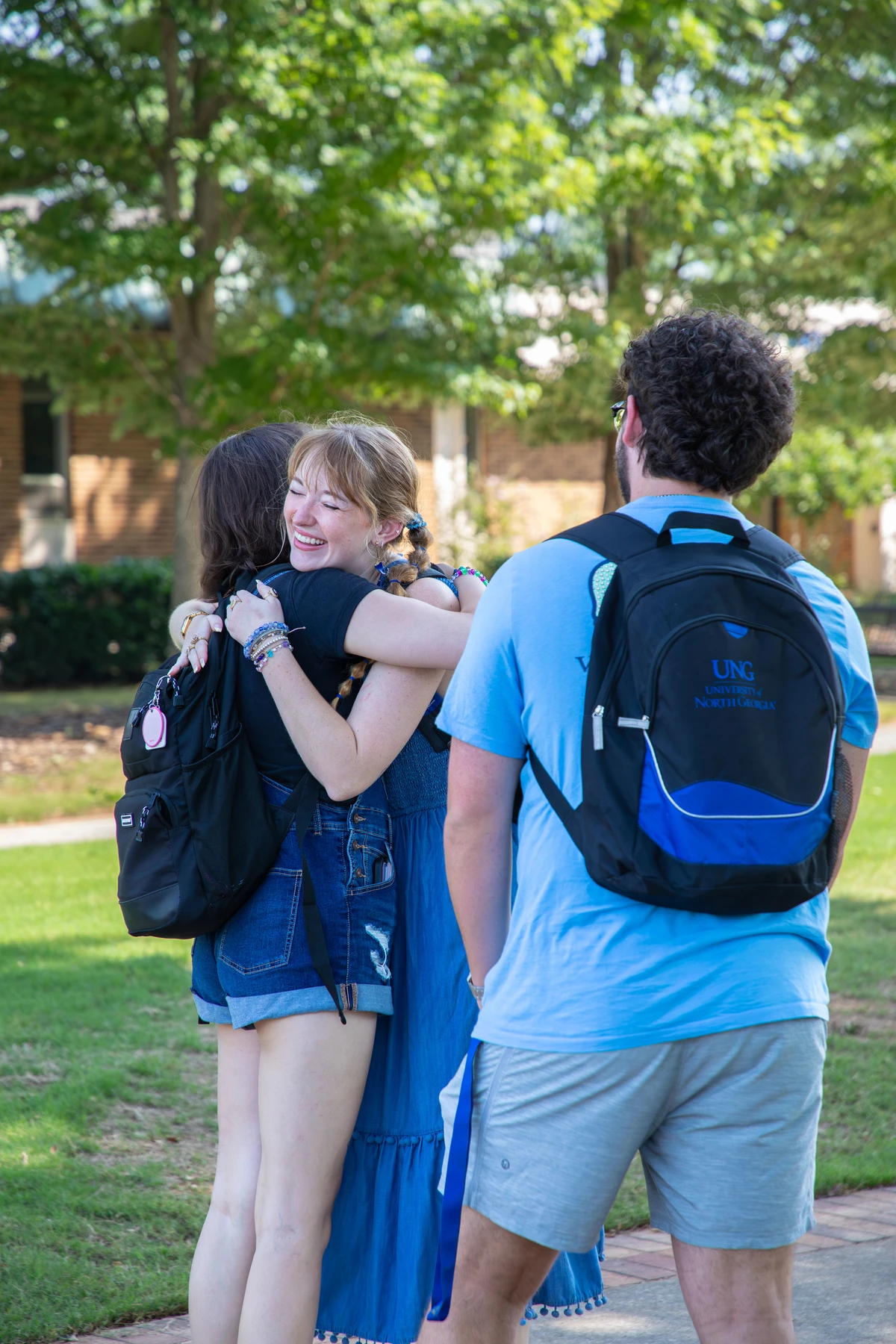 Three people wearing casual clothes hug each other.